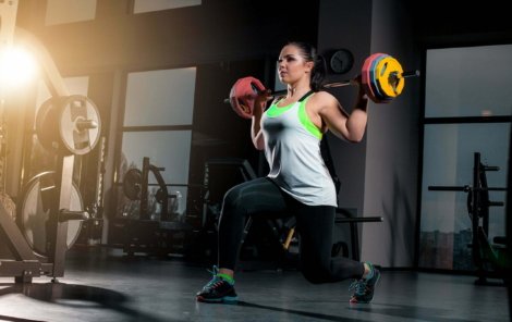Fit young woman lifting barbells looking focused, working out at a gym