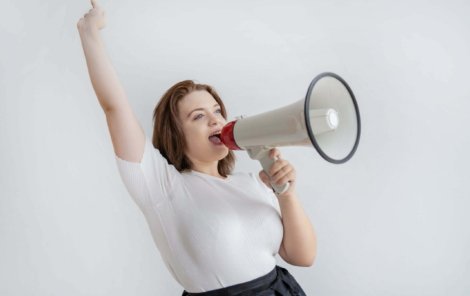 Happy excited young woman raising arm and screaming in megaphone. Emotional female business executive with loudspeaker. Communication concept