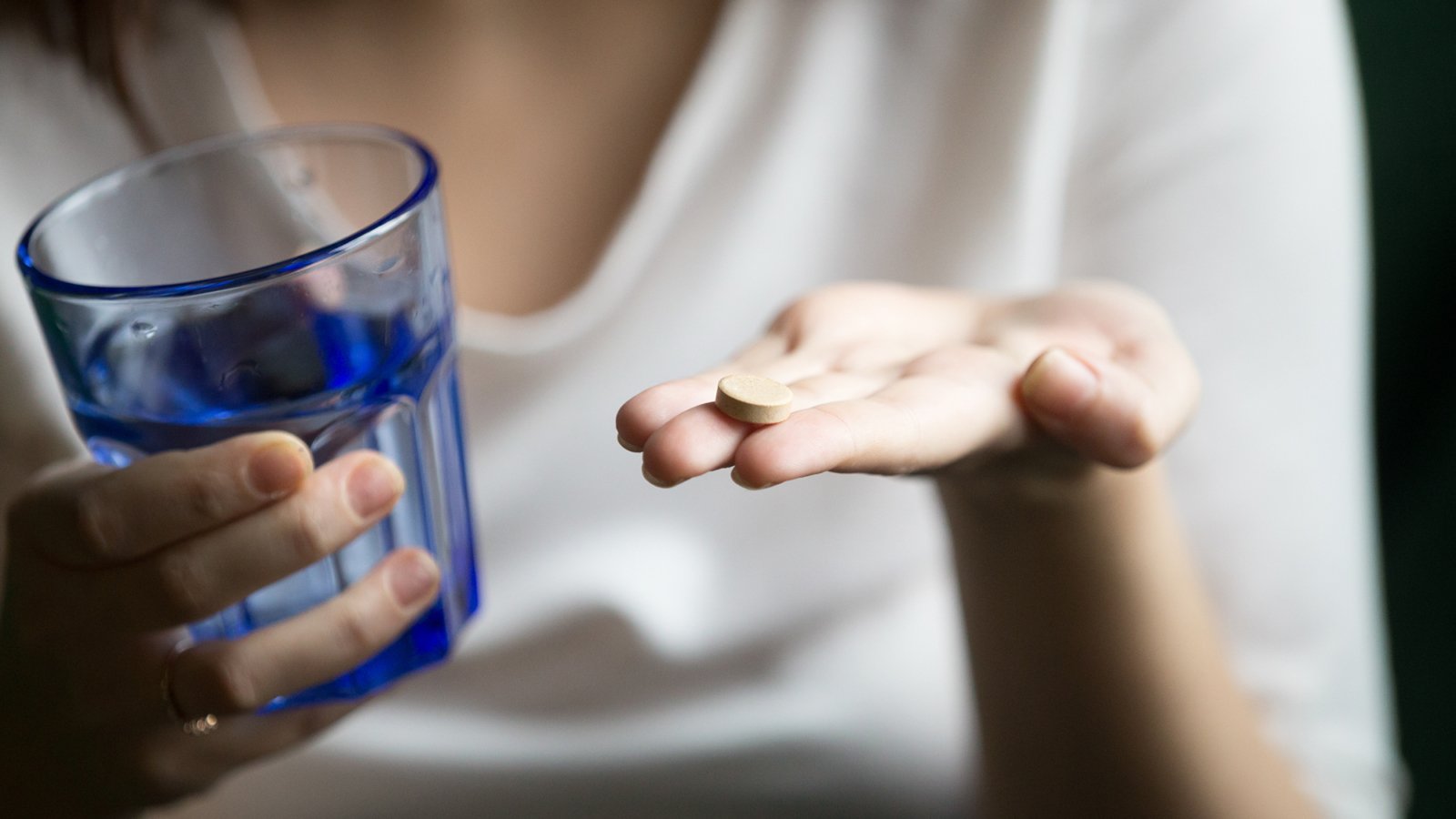 Female hands holding pill and glass of water, woman taking supplements or antibiotic antidepressant painkiller medication to relieve pain headache, contraception side effects concept, close up view