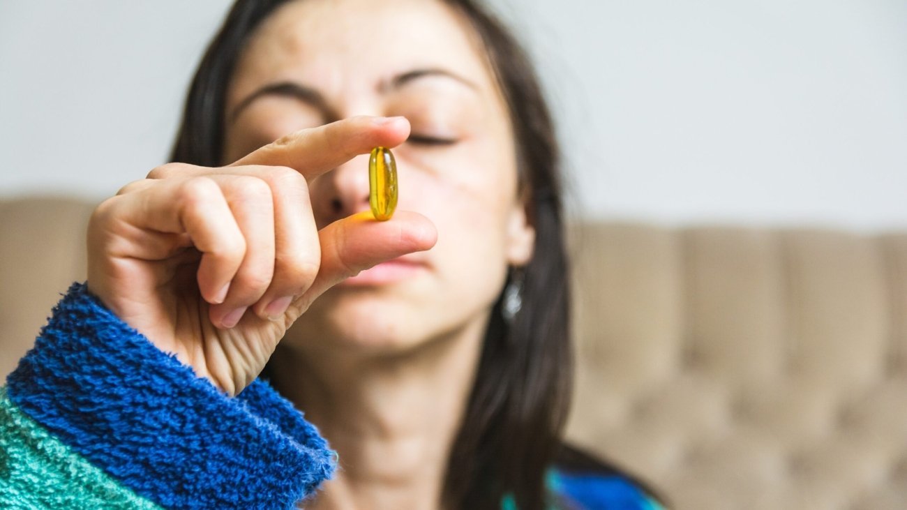 A woman holding a yellow pill in front of her face