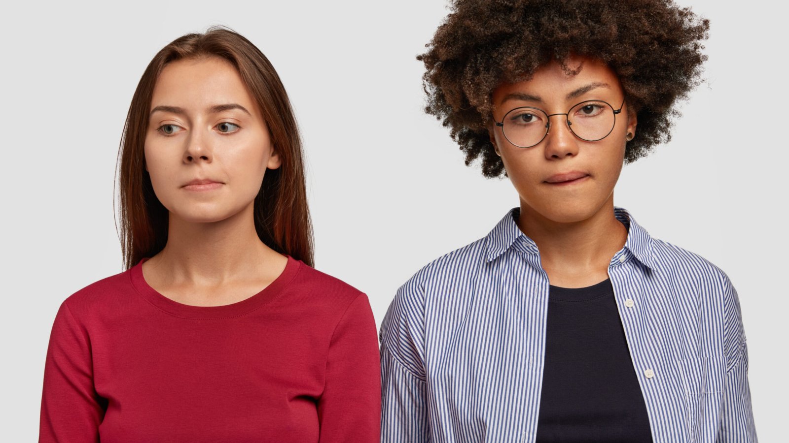 Indoor shot of contemplative mixed race women purse lips, being deep in thoughts, have sad expressions, dressed in casual clothes, isolated over white background. Facial expressions concept.