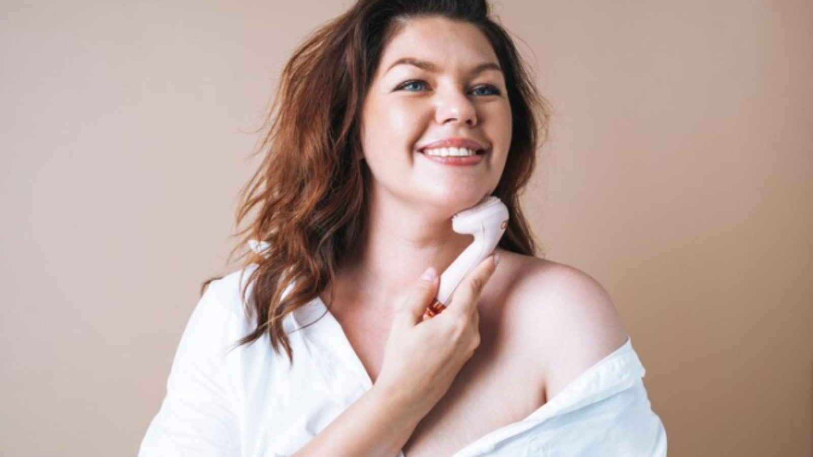 Premium-Photo-Self-loving-woman-plus-size-in-white-shirt-with-facial-massager-in-hands-on-beige-background-body-love