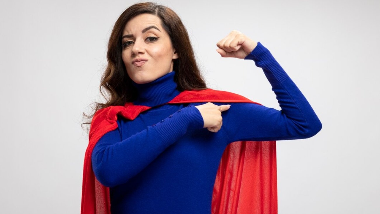 confident-caucasian-superhero-girl-with-red-cape-tenses-points-biceps-white_141793-98028